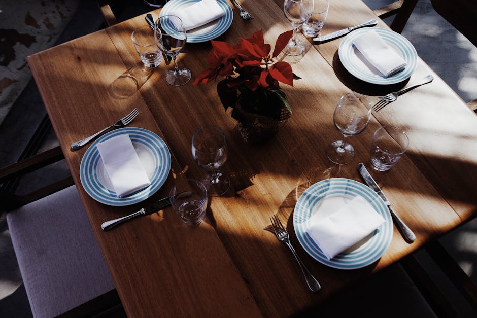 A beautifully set dining table with striped plates and silverware, centered around a red flower arrangement.